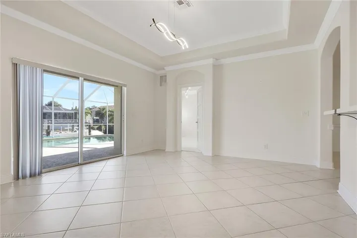 Unfurnished room with a raised ceiling, ornamental molding, a sunroom, light tile patterned floors, and arched walkways