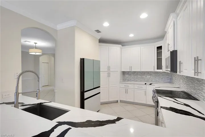 Kitchen with arched walkways, white cabinets, freestanding refrigerator, electric stove, and light tile patterned floors