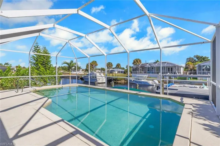 Swimming pool featuring a water view, glass enclosure, a sunroom, and a patio area