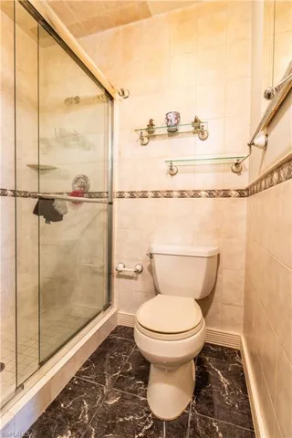 Bathroom with a shower with door, tile walls, and toilet