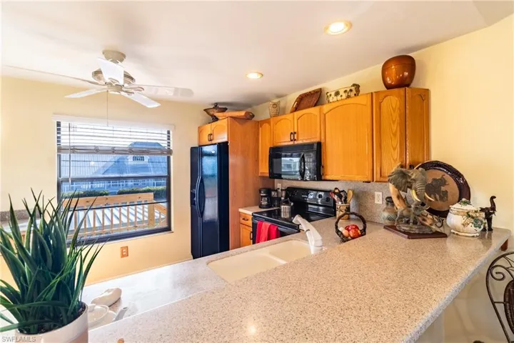 Kitchen with kitchen peninsula, decorative backsplash, ceiling fan, sink, and black appliances
