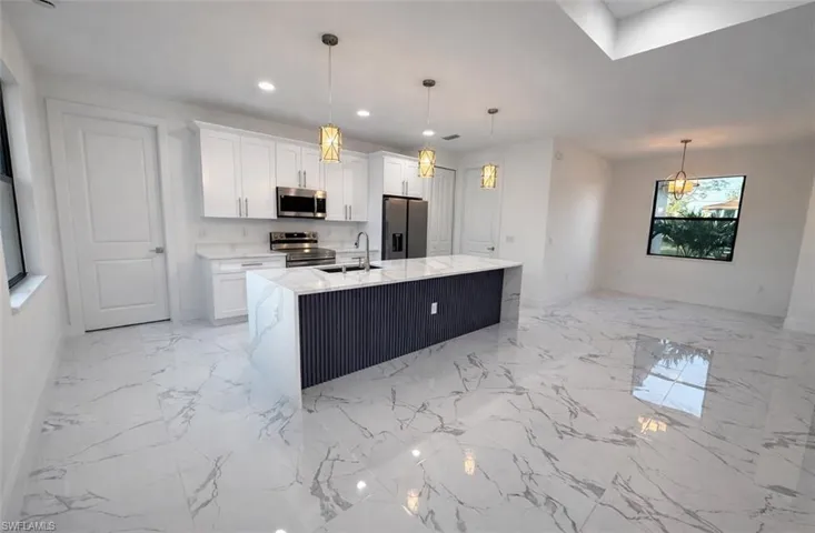 Kitchen featuring white cabinets, appliances with stainless steel finishes, an island with sink, light stone countertops, and recessed lighting