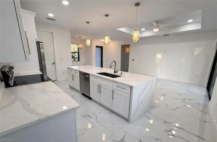 Kitchen featuring a raised ceiling, recessed lighting, light stone counters, white cabinets, and appliances with stainless steel finishes
