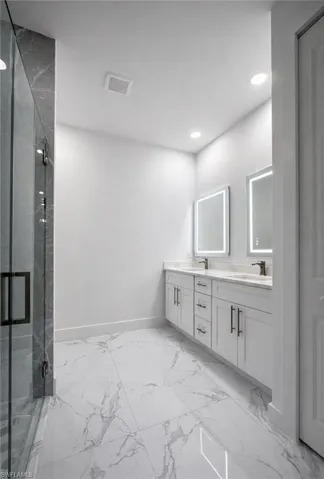 Bathroom with a marble finish shower, double vanity, recessed lighting, and light marble finish floors