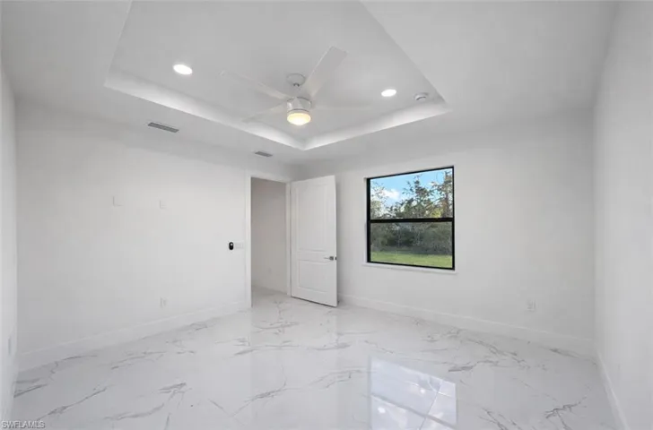 Unfurnished bedroom featuring recessed lighting, ceiling fan, a raised ceiling, and light marble finish flooring
