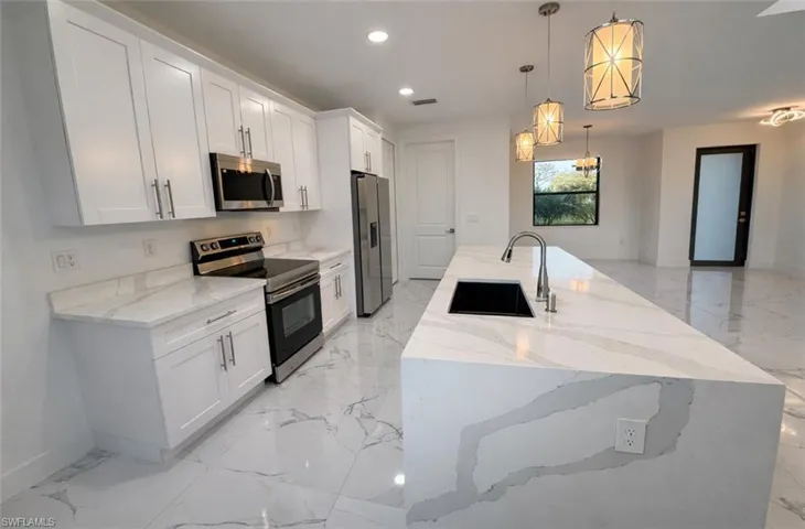 Kitchen with stainless steel appliances, light stone counters, white cabinets, a spacious island, and decorative light fixtures
