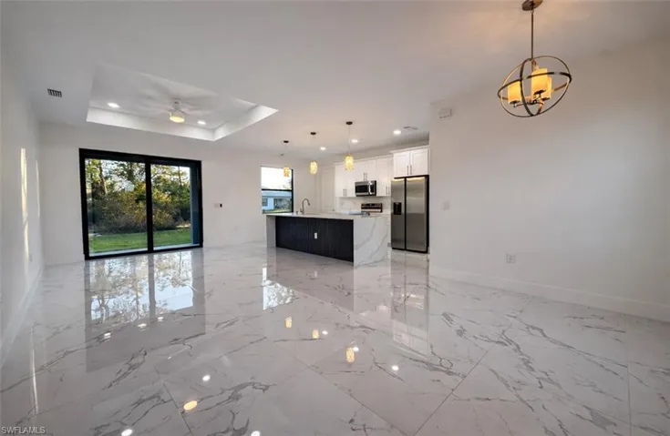 Kitchen featuring open floor plan, white cabinetry, hanging light fixtures, stainless steel appliances, and a tray ceiling
