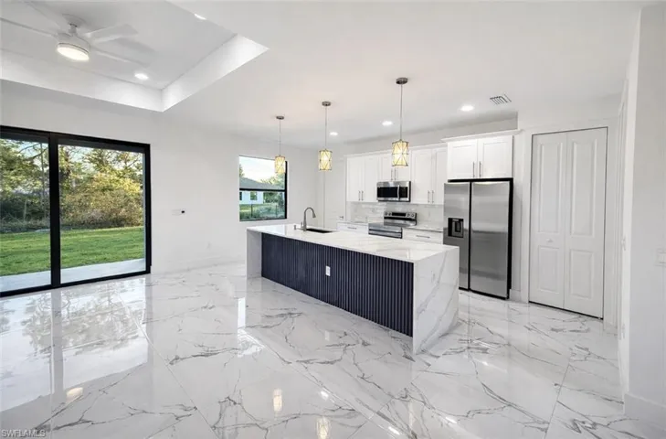 Kitchen featuring appliances with stainless steel finishes, pendant lighting, light stone countertops, a kitchen island with sink, and white cabinets