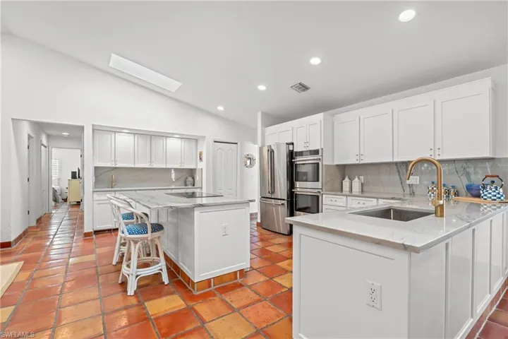 Kitchen featuring lofted ceiling, a kitchen bar, tasteful backsplash, light stone counters, and recessed lighting