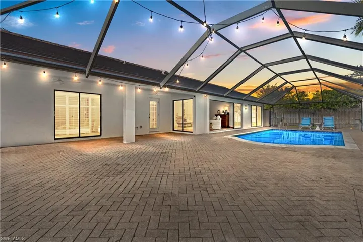 Pool at dusk with a sunroom, glass enclosure, an outdoor pool, and a patio area