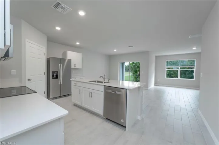 Kitchen featuring stainless steel appliances, white cabinetry, an island with sink, recessed lighting, and light stone countertops