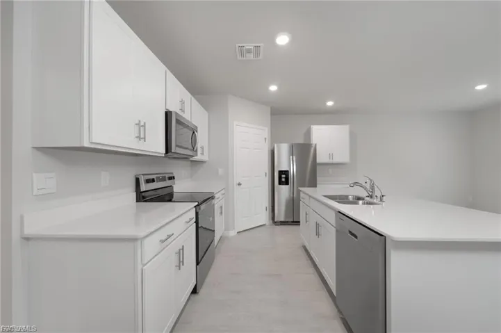Kitchen with appliances with stainless steel finishes, white cabinets, an island with sink, recessed lighting, and light stone countertops