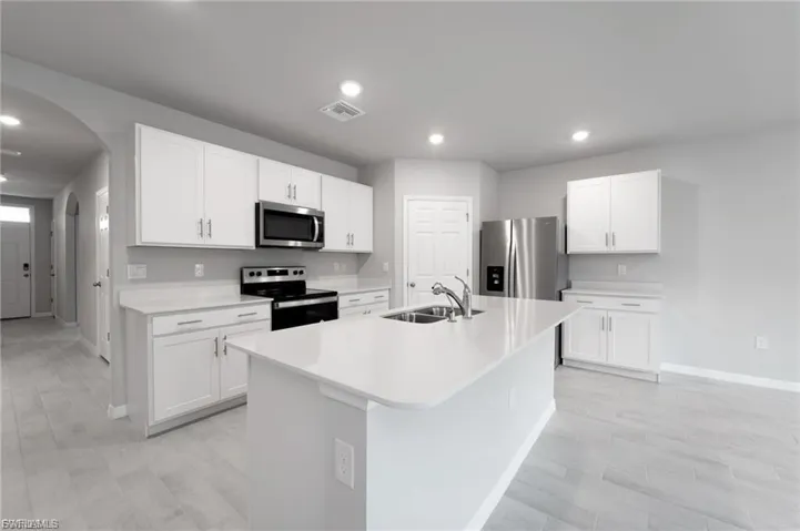 Kitchen featuring arched walkways, stainless steel appliances, white cabinetry, an island with sink, and recessed lighting