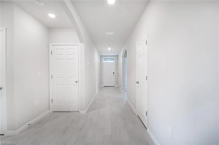 Hallway with arched walkways, light wood finished floors, and recessed lighting