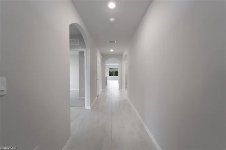 Corridor featuring arched walkways, light wood-style flooring, and recessed lighting