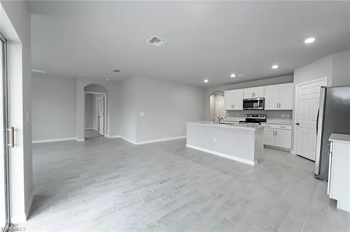 Kitchen with arched walkways, appliances with stainless steel finishes, white cabinetry, recessed lighting, and a center island with sink
