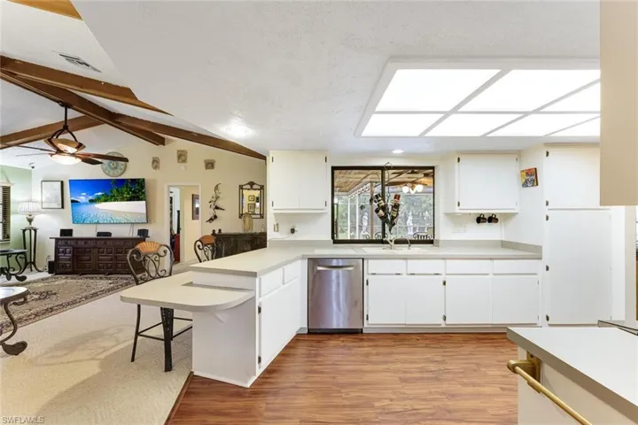 Kitchen featuring a peninsula, light wood-type flooring, stainless steel dishwasher, a textured ceiling, and light countertops