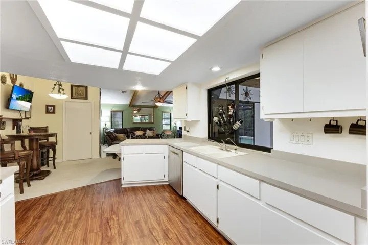 Kitchen with light countertops, wood finished floors, open floor plan, dishwasher, and white cabinets