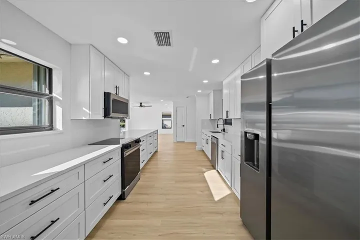 Kitchen with stainless steel appliances, white cabinetry, recessed lighting, light stone counters, and light wood-style floors