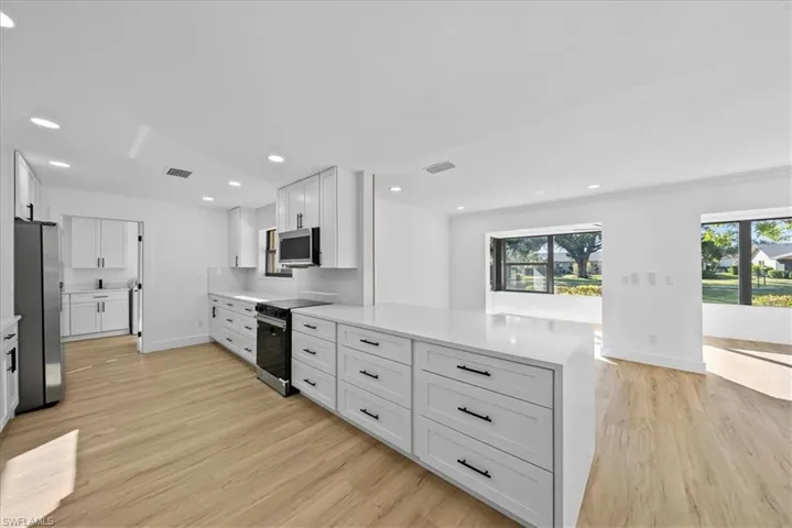 Kitchen featuring white cabinets, stainless steel appliances, recessed lighting, light wood-style floors, and light stone countertops