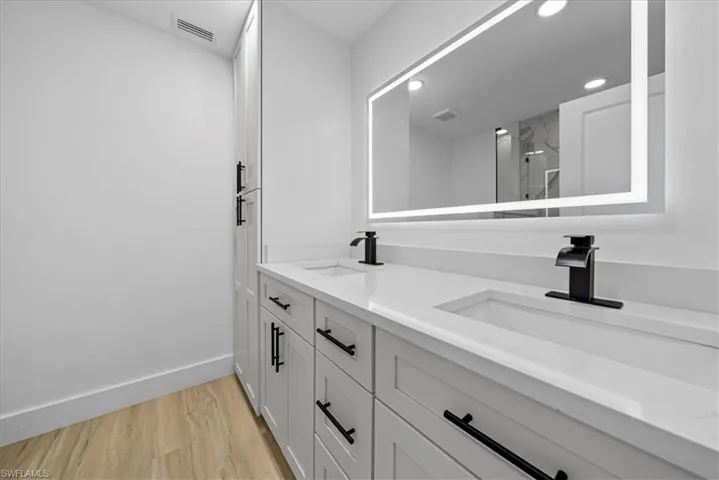 Full bath with a marble finish shower, double vanity, light wood-style floors, and recessed lighting