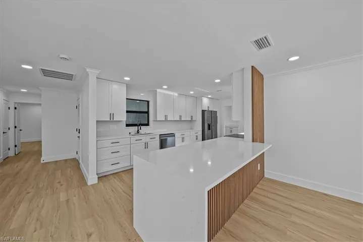 Kitchen featuring white cabinets, ornamental molding, light stone counters, light wood finished floors, and stainless steel appliances