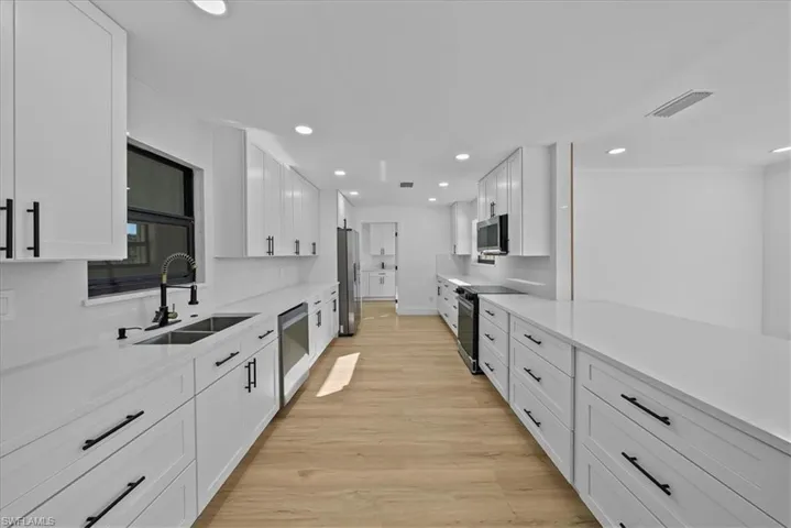 Kitchen featuring white cabinets, light stone counters, stainless steel appliances, light wood-style floors, and recessed lighting