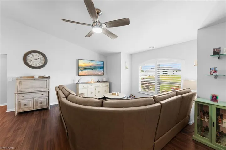 Living room featuring vaulted ceiling, a ceiling fan, and dark wood-style flooring