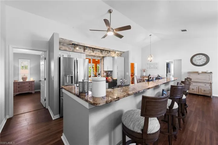 Kitchen with dark wood finished floors, vaulted ceiling, stainless steel refrigerator with ice dispenser, ceiling fan, and healthy amount of natural light