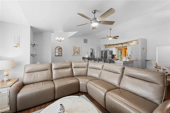 Living room featuring vaulted ceiling, a ceiling fan, a chandelier, and wood finished floors