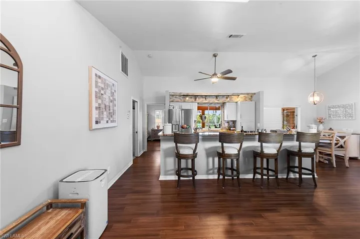 Kitchen featuring lofted ceiling, dark wood-type flooring, a kitchen breakfast bar, a ceiling fan, and stainless steel fridge with ice dispenser