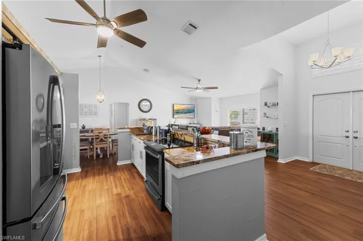 Kitchen featuring stainless steel appliances, a ceiling fan, vaulted ceiling, wood finished floors, and a chandelier
