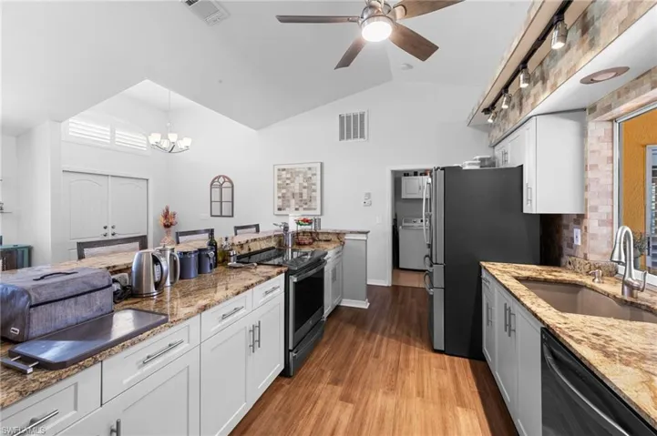 Kitchen with vaulted ceiling, appliances with stainless steel finishes, light wood-type flooring, a ceiling fan, and white cabinets