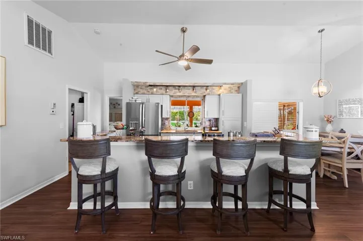 Kitchen featuring stainless steel refrigerator with ice dispenser, ceiling fan, dark wood finished floors, a breakfast bar, and hanging light fixtures