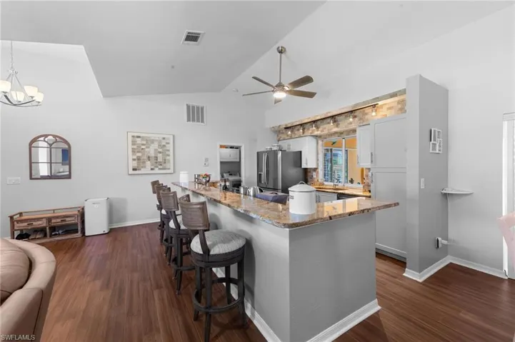 Kitchen with dark wood-style flooring, a kitchen breakfast bar, light stone countertops, white cabinets, and high vaulted ceiling