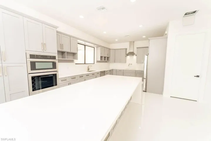 Kitchen featuring recessed lighting, wall chimney range hood, stainless steel appliances, gray cabinetry, and open shelves