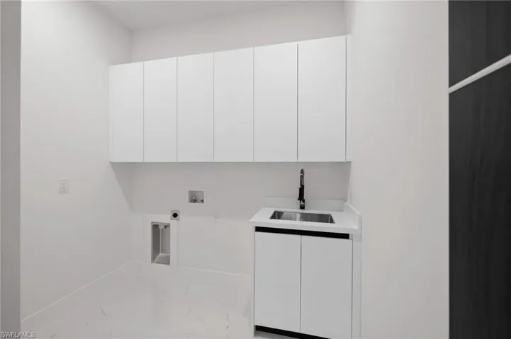 Washroom featuring cabinet space, marble look tiles, hookup for an electric dryer, washer hookup, and baseboards