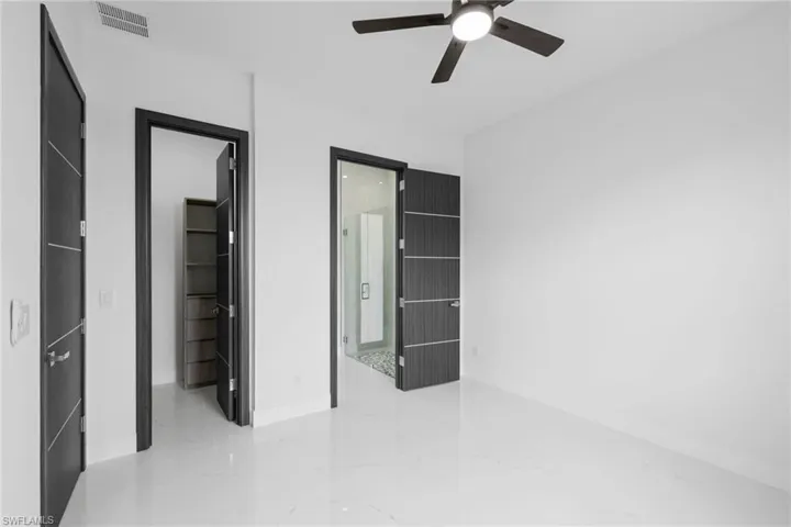 Unfurnished bedroom with baseboards, a ceiling fan, light marble finish flooring, ensuite bathroom, and a walk in closet