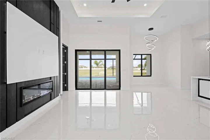 Unfurnished living room with marble tiled floors, recessed lighting, a glass covered fireplace, and a raised ceiling