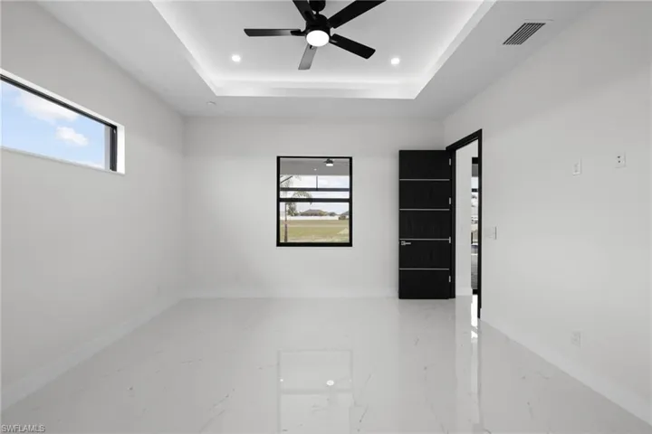 Unfurnished room featuring light marble finish floors, a ceiling fan, recessed lighting, a tray ceiling, and baseboards