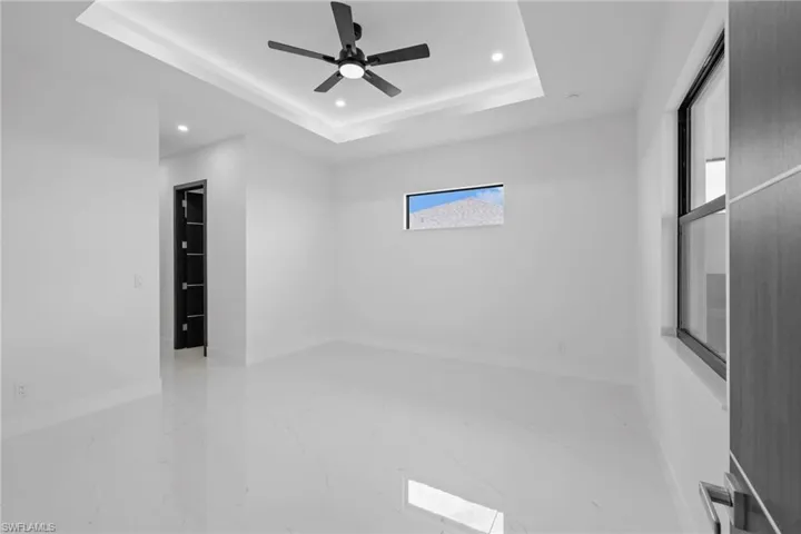 Unfurnished room featuring marble tiled floors, recessed lighting, a raised ceiling, a ceiling fan, and baseboards