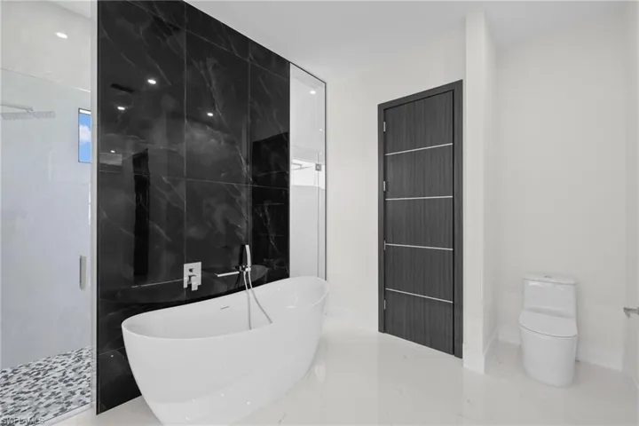 Bathroom featuring a freestanding tub, marble tiled flooring, toilet, a shower stall, and baseboards