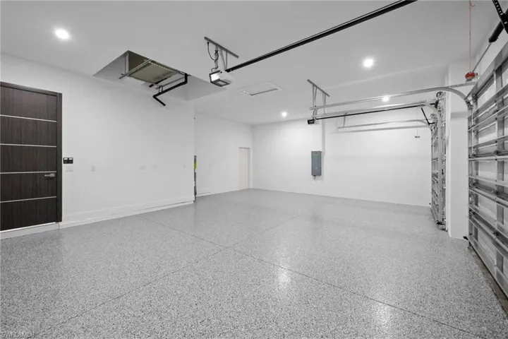 Garage with a garage door opener, recessed lighting, and electric panel