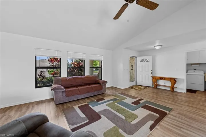 Living room featuring ceiling fan, hardwood / wood-style floors, high vaulted ceiling, and washer / dryer