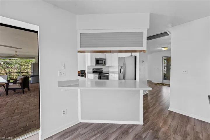 Kitchen with kitchen peninsula, appliances with stainless steel finishes, ceiling fan, white cabinets, and hardwood / wood-style floors