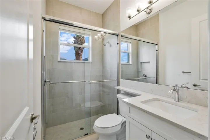 Bathroom with a shower with shower door, vanity with extensive cabinet space, and toilet