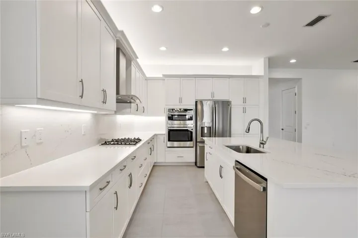 Kitchen with appliances with stainless steel finishes, wall chimney range hood and an island with sink
