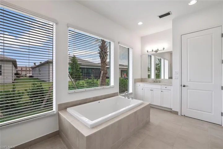 Master Bathroom with vanity with extensive cabinet space, tiled bath, and tile floors
