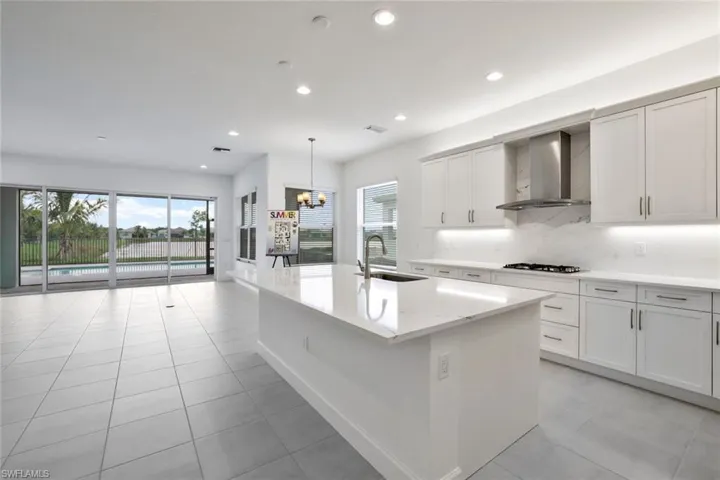 Kitchen with light tile floors, wall chimney exhaust hood, a kitchen island with sink