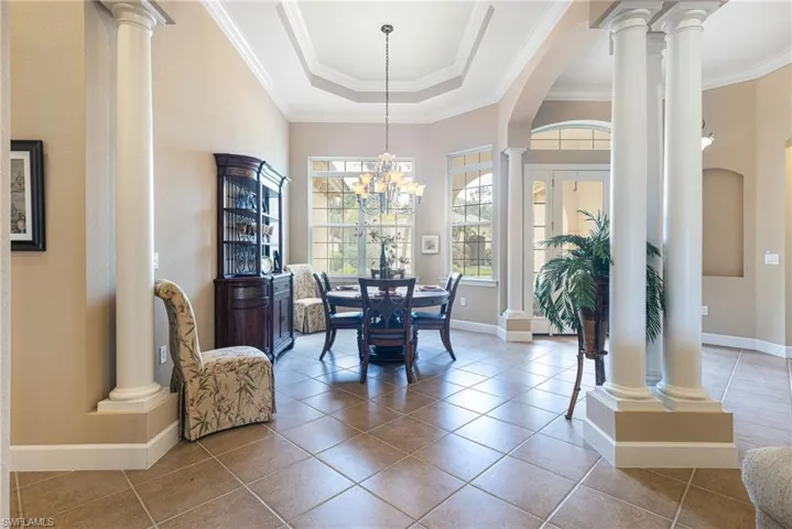 Tiled dining room featuring crown molding, baseboards, a tray ceiling, decorative columns, and arched walkways